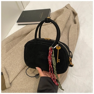 Détail d'un sac bowling en daim noir avec ferrures dorées et pendentif clé décoratif
