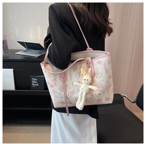 Detail of white tote bag with pink trim and bunny pendant shown on shoulder
