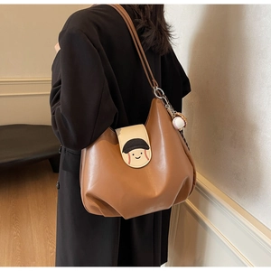 Detail of a brown Hobo backpack featuring a cartoon smiley face and baseball pendant accessory