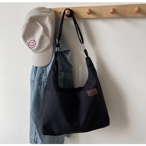 Détail du grand sac cabas noir en toile avec étiquette en cuir sur un support en bois
