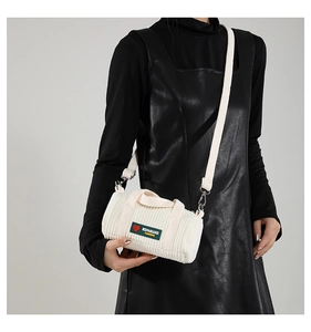 Detail of white corduroy cylinder bag featuring green logo patch and wide strap