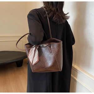 Detail einer dunkelbraunen Leder-Shopper-Tasche mit dekorativem Seidenschal am Griff