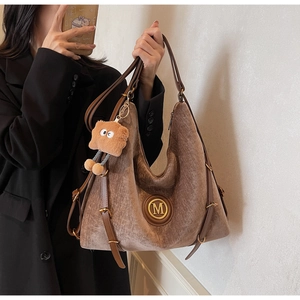 Detail of a brown velvet tote bag featuring a gold M logo and leather straps with buckles