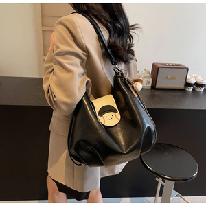 Close-up of black leather tote with baseball smiley pattern on a model in a cozy cafe
