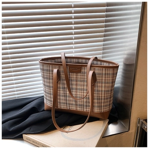 Detail view of plaid tote bag featuring brown leather trim and metallic brand plaque