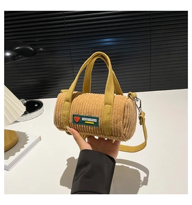 Detail of yellow corduroy cylinder bag featuring fashion label and metal hardware