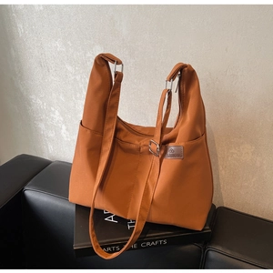 Détail du grand cabas orange avec bandoulière large et écusson logo en cuir sur le devant