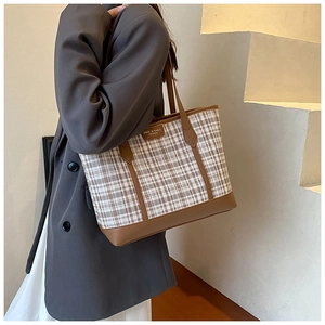 Detail of checkered canvas tote bag with brown leather straps worn by model on shoulder