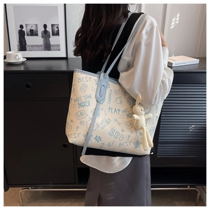Detail of cream tote bag with blue graffiti prints and plush rabbit charm on a shoulder strap