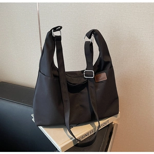 Détail du sac fourre-tout noir en toile avec poche latérale et étiquette sur des livres