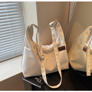Détail de la bandoulière réglable et du patch logo en cuir sur le sac cabas en toile écru