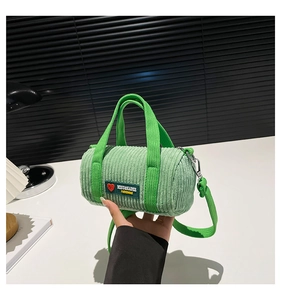 Detail shot of light green corduroy barrel bag featuring logo patch and strap accents