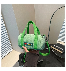 Close-up of green corduroy cylindrical bag with leather tag and woven handles