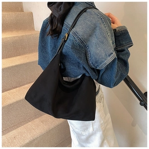 Model trägt eine große schwarze Hobo-Tasche aus mattem Stoff mit verstellbarem Gurt