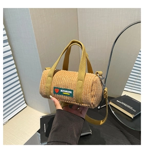 Detailed macro view of yellow corduroy cylinder bag with embroidered logo and hand-held strap