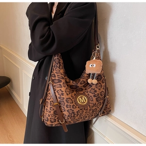 Detail of leopard print tote bag with brown leather strap and fuzzy monster charm