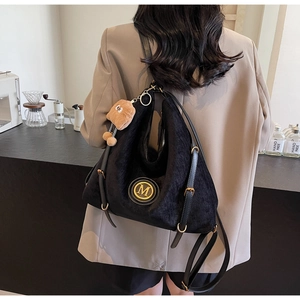 Detail of black corduroy tote bag with gold M logo and brown plush charm on model