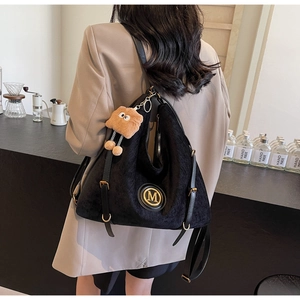 Close-up of black corduroy tote bag with golden M logo and fuzzy monster charm