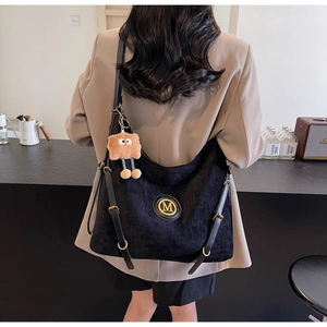 Detail of black velvet tote bag featuring a gold M emblem and a cute plush bear charm