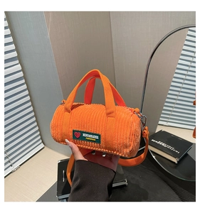 Detail of orange corduroy barrel bag featuring a green woven label and metal hardware