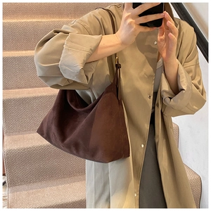 Lifestyle-Foto einer dunkelbraunen Wildleder-Hobo-Tasche auf der Schulter auf einer Treppe