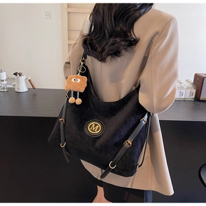 Detail of black corduroy tote bag showing gold M logo and leather buckled straps
