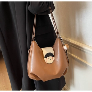 Close-up of brown leather tote bag featuring a smiling face and baseball glove charm