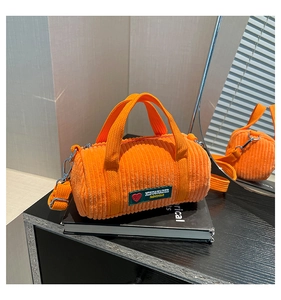 Detail of orange corduroy barrel bag with dark green logo patch and metal buckle