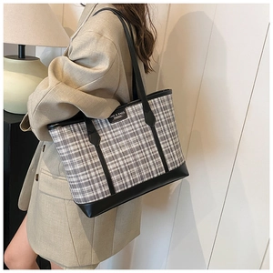 Detailed view of checkered tote bag with black leather trim worn on a female shoulder
