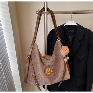 Close-up of brown velvet tote bag featuring a leather strap and metallic M logo detail