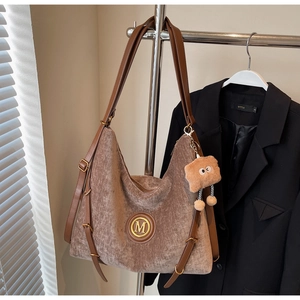 Detail of brown corduroy tote bag with M logo and plush toast charm on metal rack