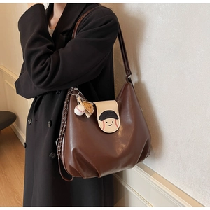 Detail of brown leather hobo bag featuring a cartoon face and baseball glove charm