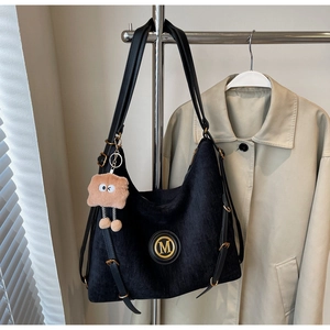 Detail of black velvet tote bag with golden M logo and brown plush pendant on a metal hanger