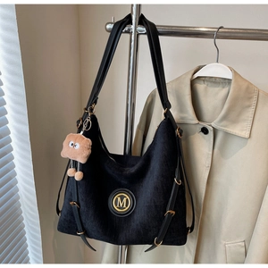 Detail of black canvas tote bag with gold M logo and cute bread-shaped charm