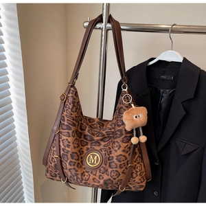 Detail of leopard print hobo bag with gold M logo and plush charm on black blazer