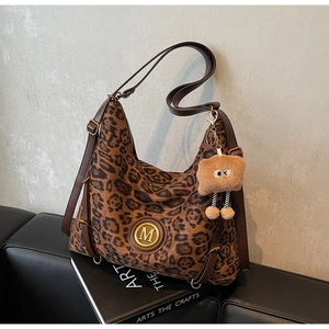 Detail of leopard print hobo bag featuring leather strap and a plush bear charm