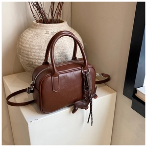 Close-up of vintage brown Boston bag with unique decorative charms on a minimalist stand