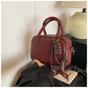 Detailed view of burgundy faux leather Boston bag with dog and chocolate charms