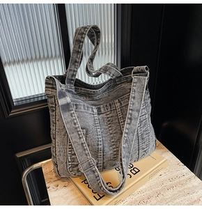 Detail of gray washed denim tote bag with visible stitching and adjustable strap on a table