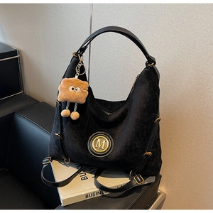 Close-up of black tote bag with gold metal M logo and brown plush toast charm detail