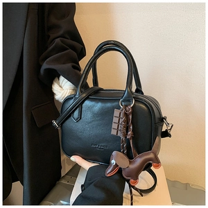 Detail of black Boston handbag with textured leather and creative puppy bag charm