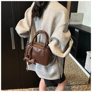 Detailed view of a brown vintage Boston bag with a leather dog charm on a gray sweatshirt