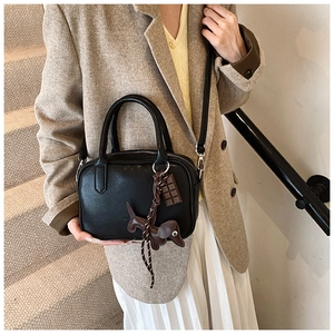 Detail of black leather Boston bag featuring dog and chocolate charms on model's shoulder