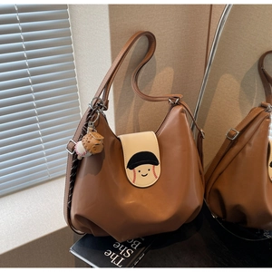 Detail of a brown leather hobo bag featuring a white flap with a baseball smile embroidery