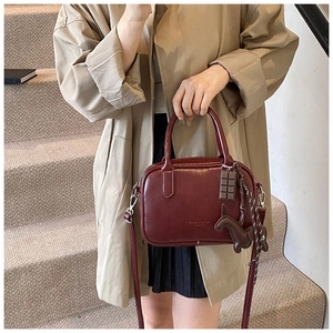 Detail of burgundy Boston bag with smooth leather finish and decorative pony charms