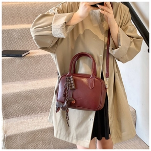Detail of dark red leather boston bag with chocolate charm and puppy pendant