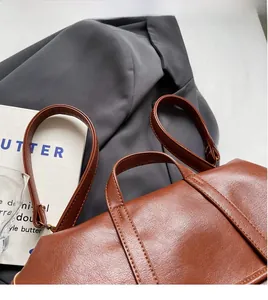Detail shot of brown leather backpack featuring reinforced stitching on handle and strap