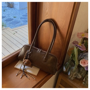 Detail of dark brown leather underarm bag with plush bear charm and braided tassel decor