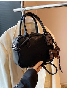 Black vintage Boston handbag with a dog charm and chocolate pendant on a beige blazer background