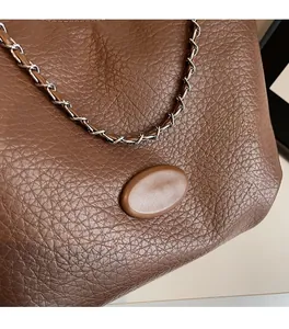 Detail of brown lychee grain leather texture and metallic chain shoulder strap on a tote bag